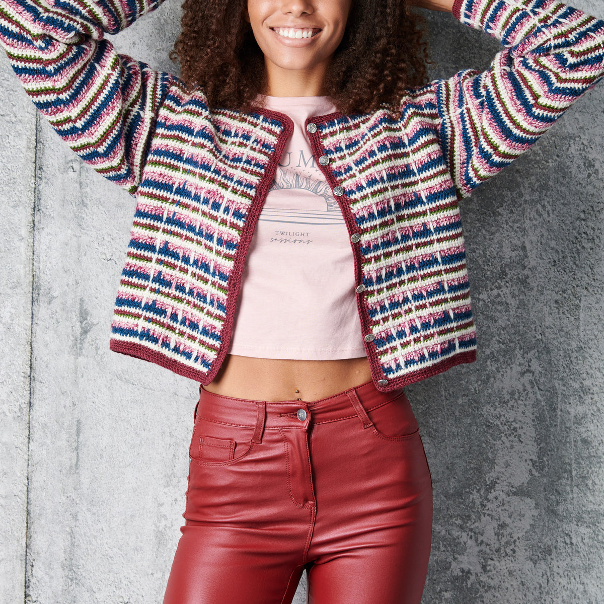 Person wearing a colorful striped cardigan and red pants against a gray background