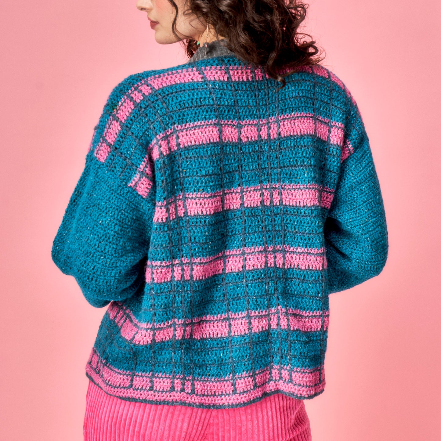 Person wearing a blue and pink striped crochet cardigan on a pink background