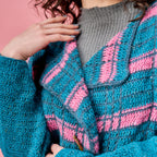 Close-up of a person wearing a blue and pink crocheted cardigan against a pink background