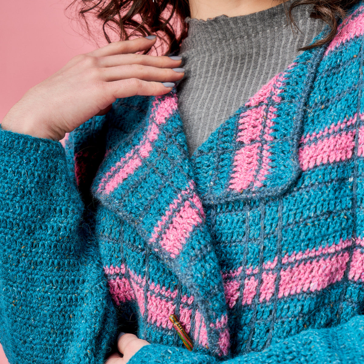Close-up of a person wearing a blue and pink crocheted cardigan against a pink background