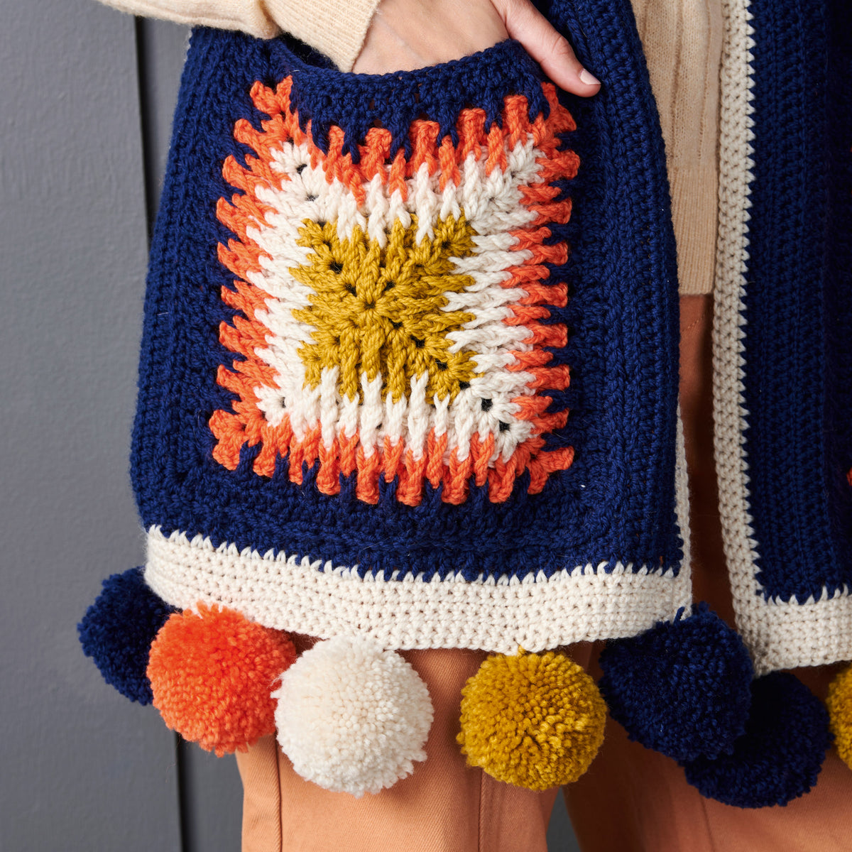 Colorful crochet skirt with pom-poms held by a person against a neutral background