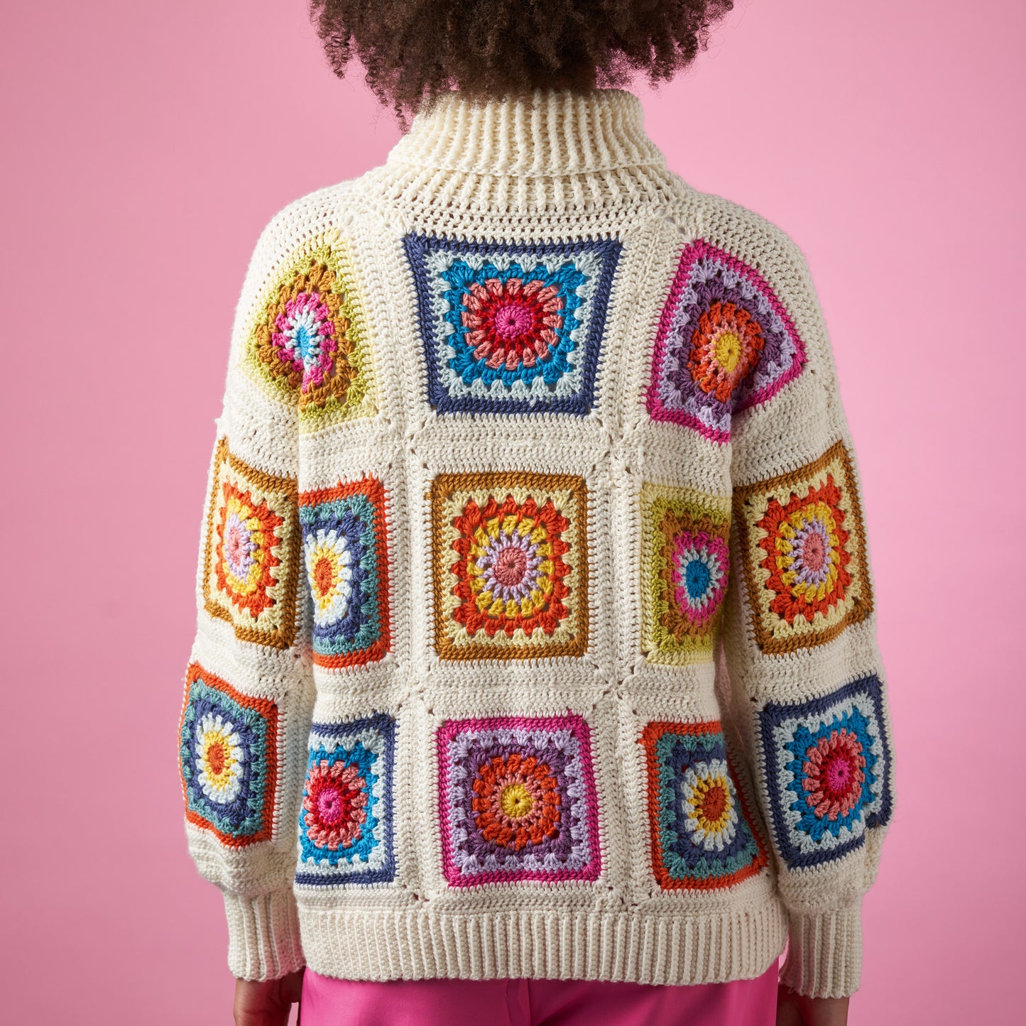 Person wearing a colorful crochet sweater with a pink background