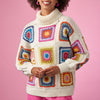 Person wearing a colorful crochet sweater against a pink background