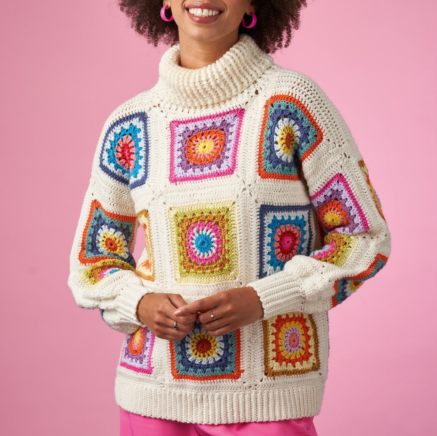 Person wearing a colorful crochet sweater against a pink background