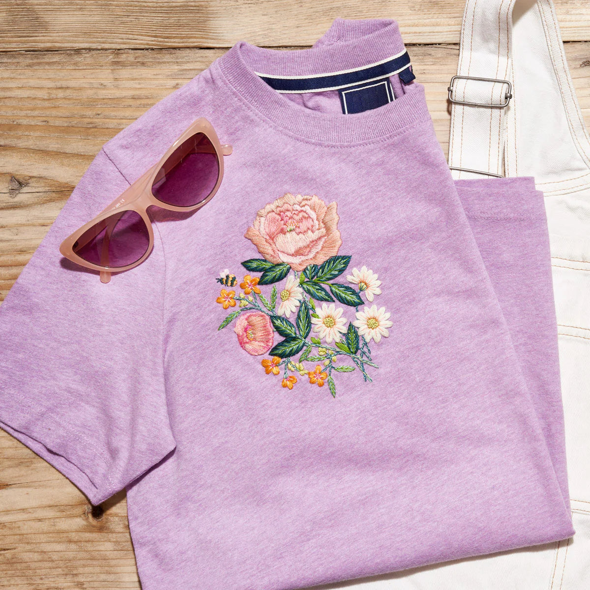 Purple sweatshirt with floral embroidery and sunglasses on a wooden surface