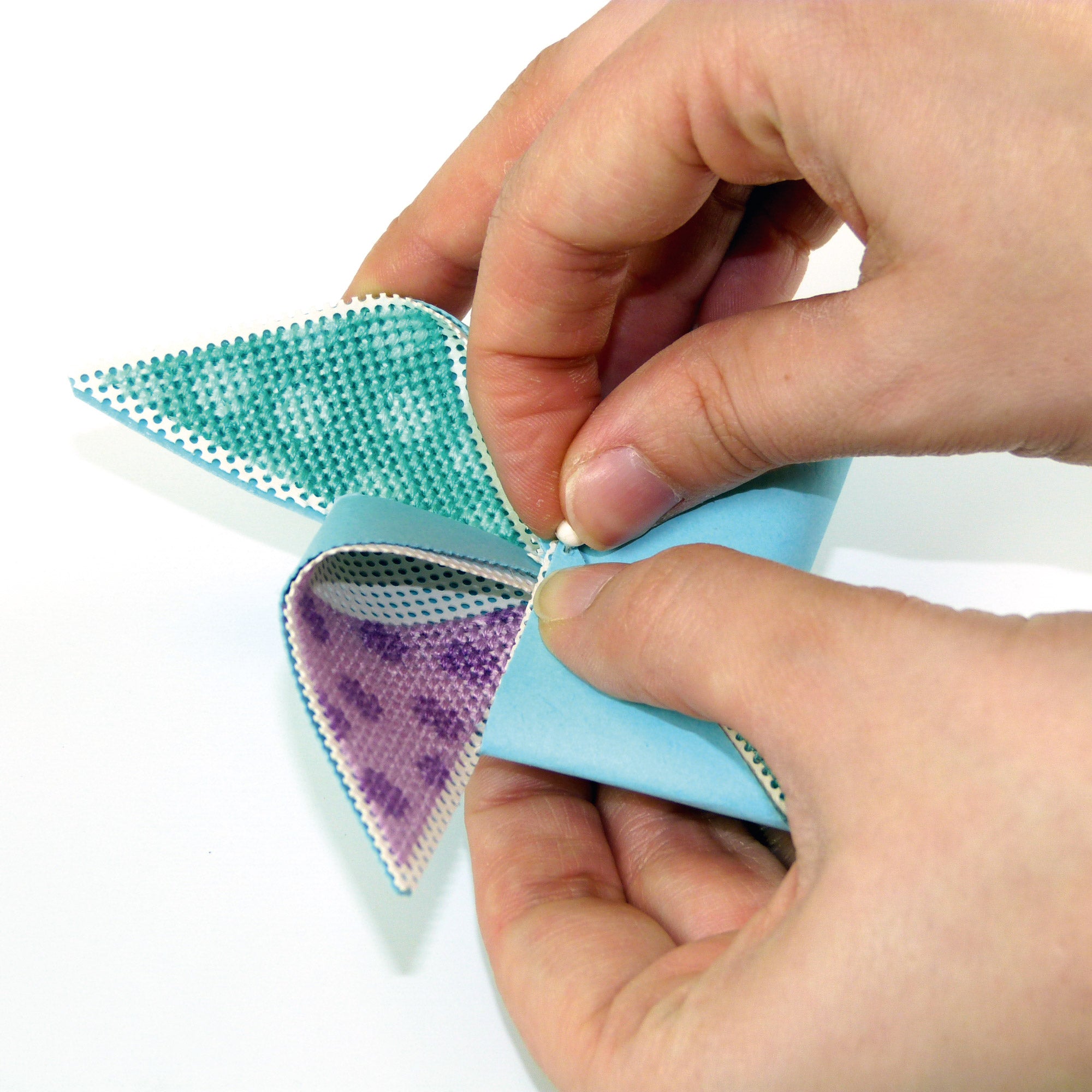 Hands folding a blue and green paper triangle with a purple pattern on a white background