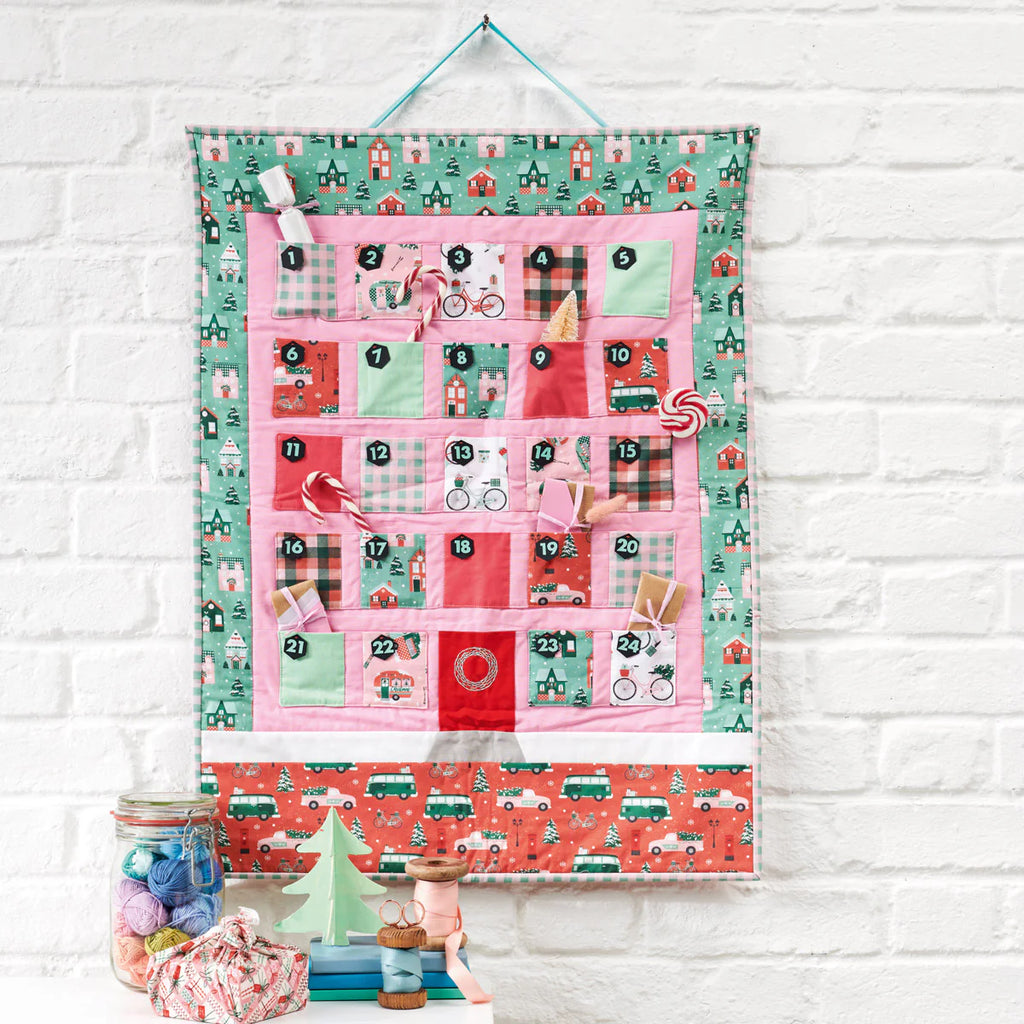 Colorful advent calendar with various patterns and numbers on a white brick wall background.