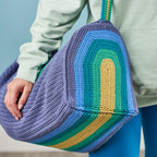 Person holding a colorful crocheted bag with a gradient of blue, green, and yellow.