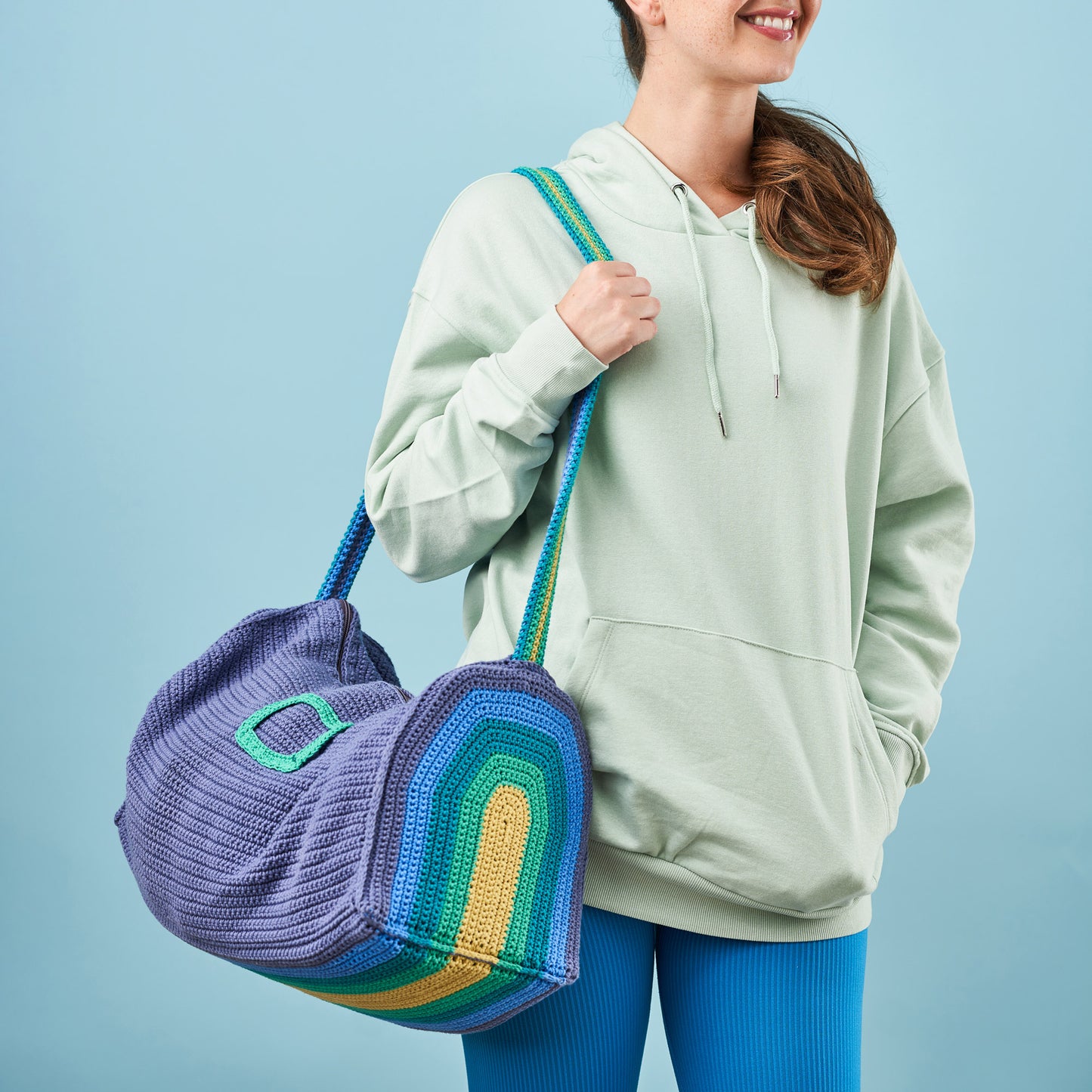 Person holding a colorful crochet bag against a light blue background
