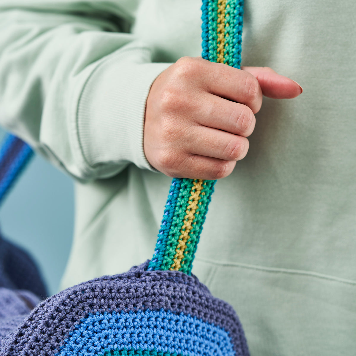 Hand holding a blue and green crocheted bag with a blurred background