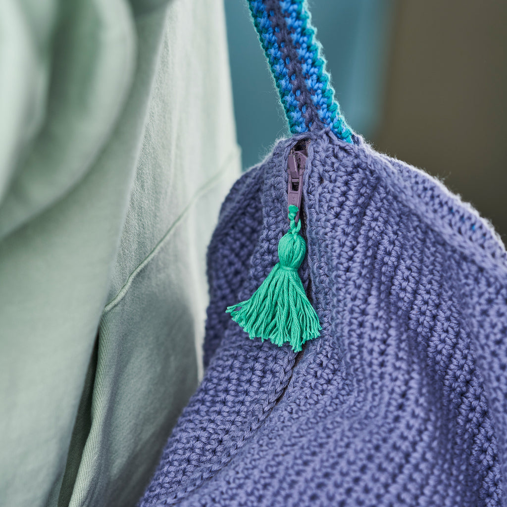 Close-up of a blue crochet bag with a green tassel against a blurred background