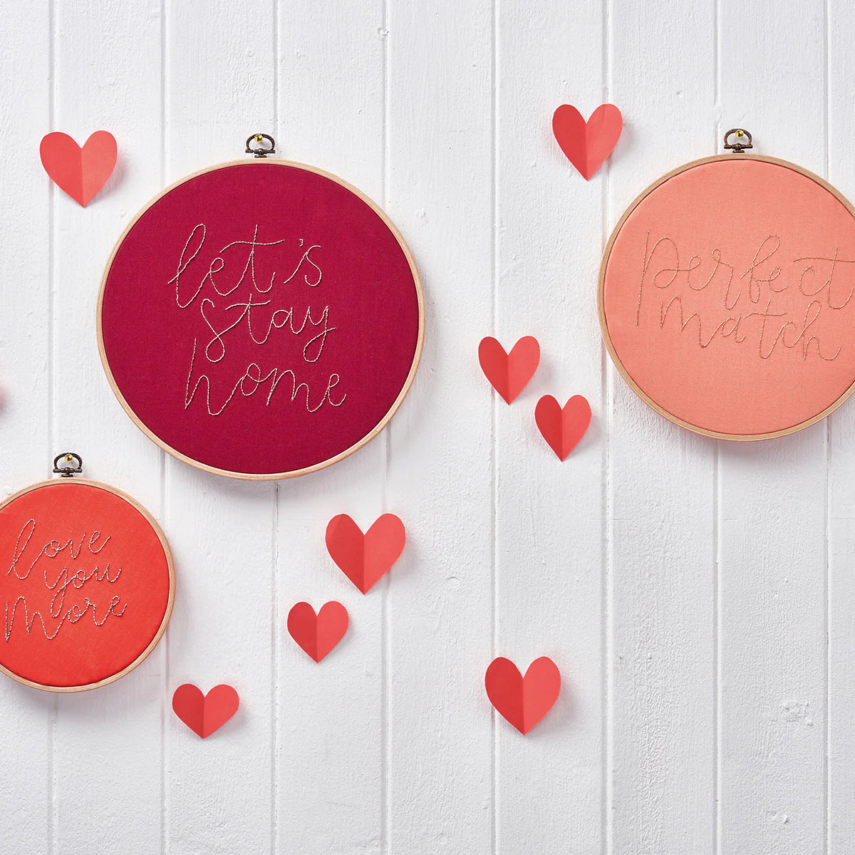 Decorative embroidery hoops with text and red hearts on a white wooden background