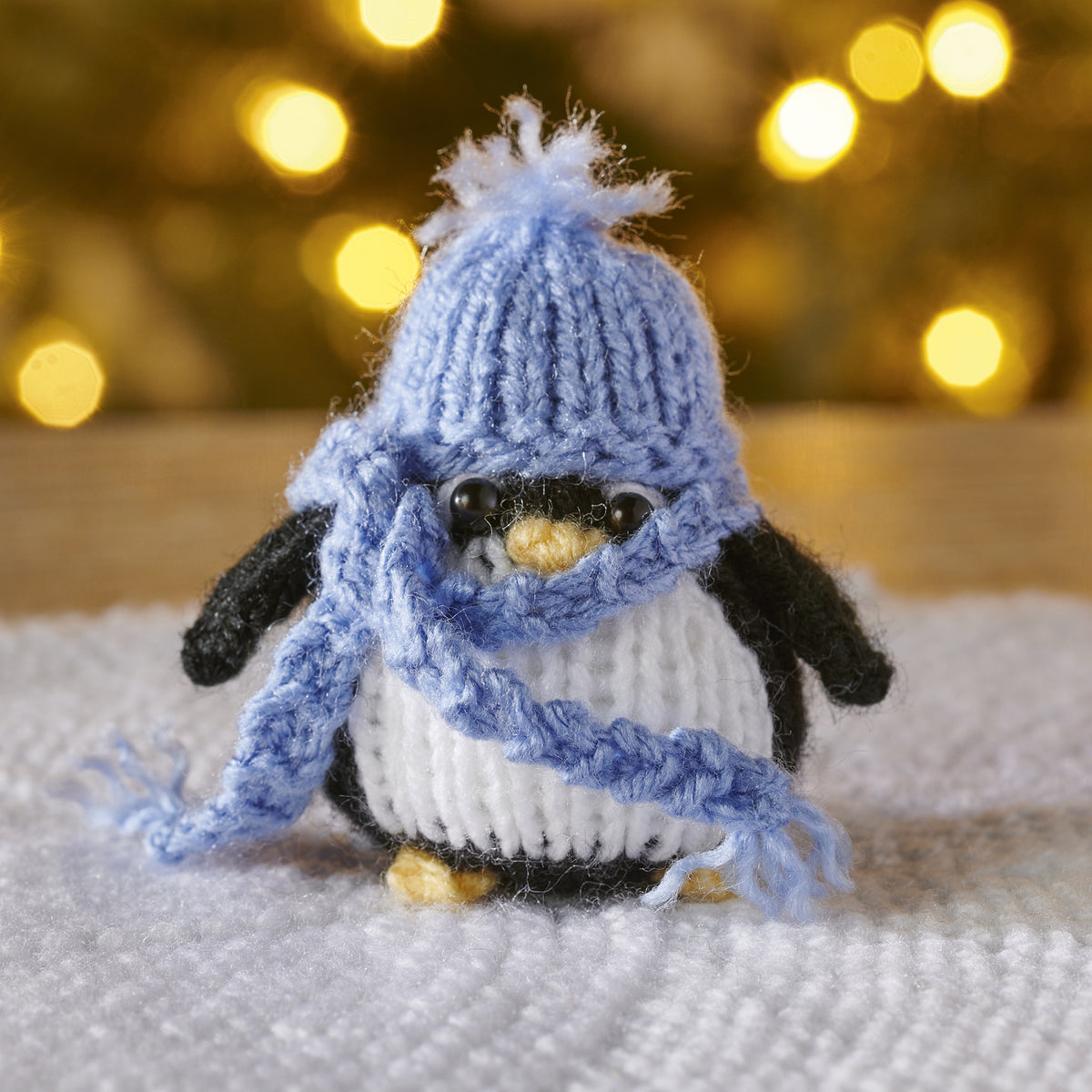 Knitted penguin toy wearing a blue scarf and hat against a blurred light background