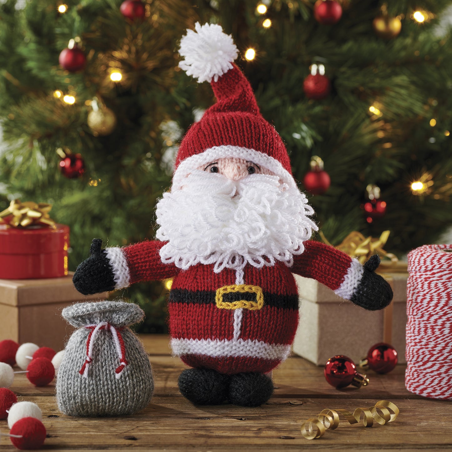 Knitted Santa Claus figure with a sack in front of a decorated Christmas tree.