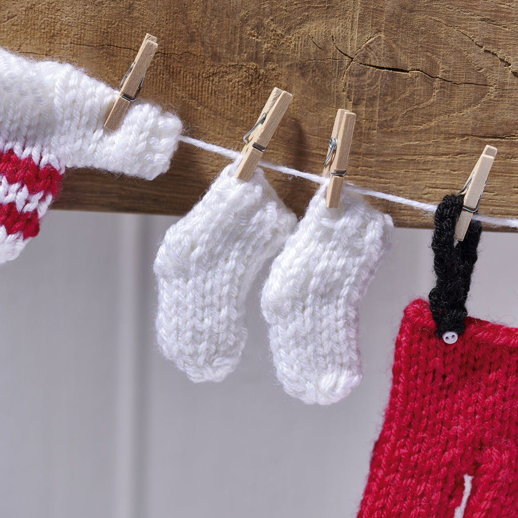 Knitted santa clothing  items including socks and a hat hanging on a line with clothespins against a wooden background.