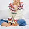 Woman wearing a colorful crochet sweater sitting on a white surface