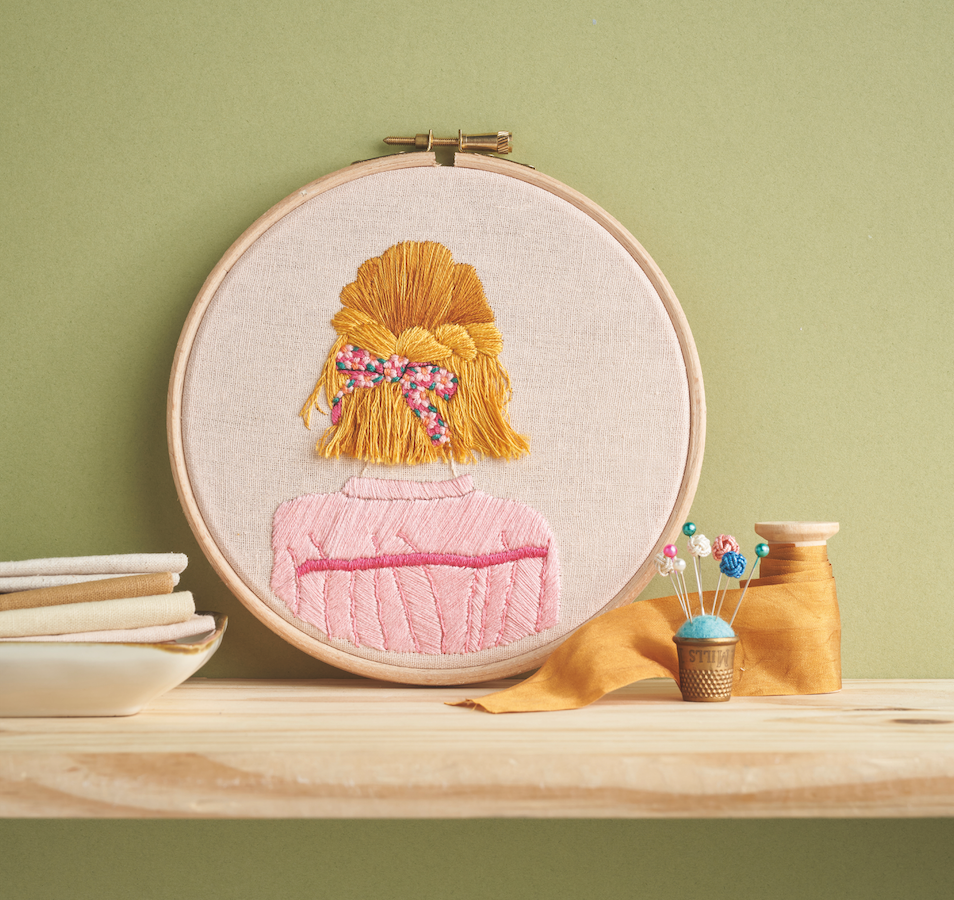 Embroidery hoop with a girl's portrait on a wooden surface against a green wall
