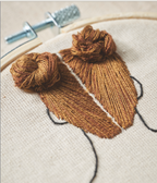 Embroidery hoop with brown yarn and a needle on a beige fabric background