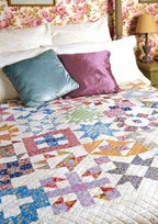 A quilt with various colorful geometric patterns displayed on a bed with decorative pillows.