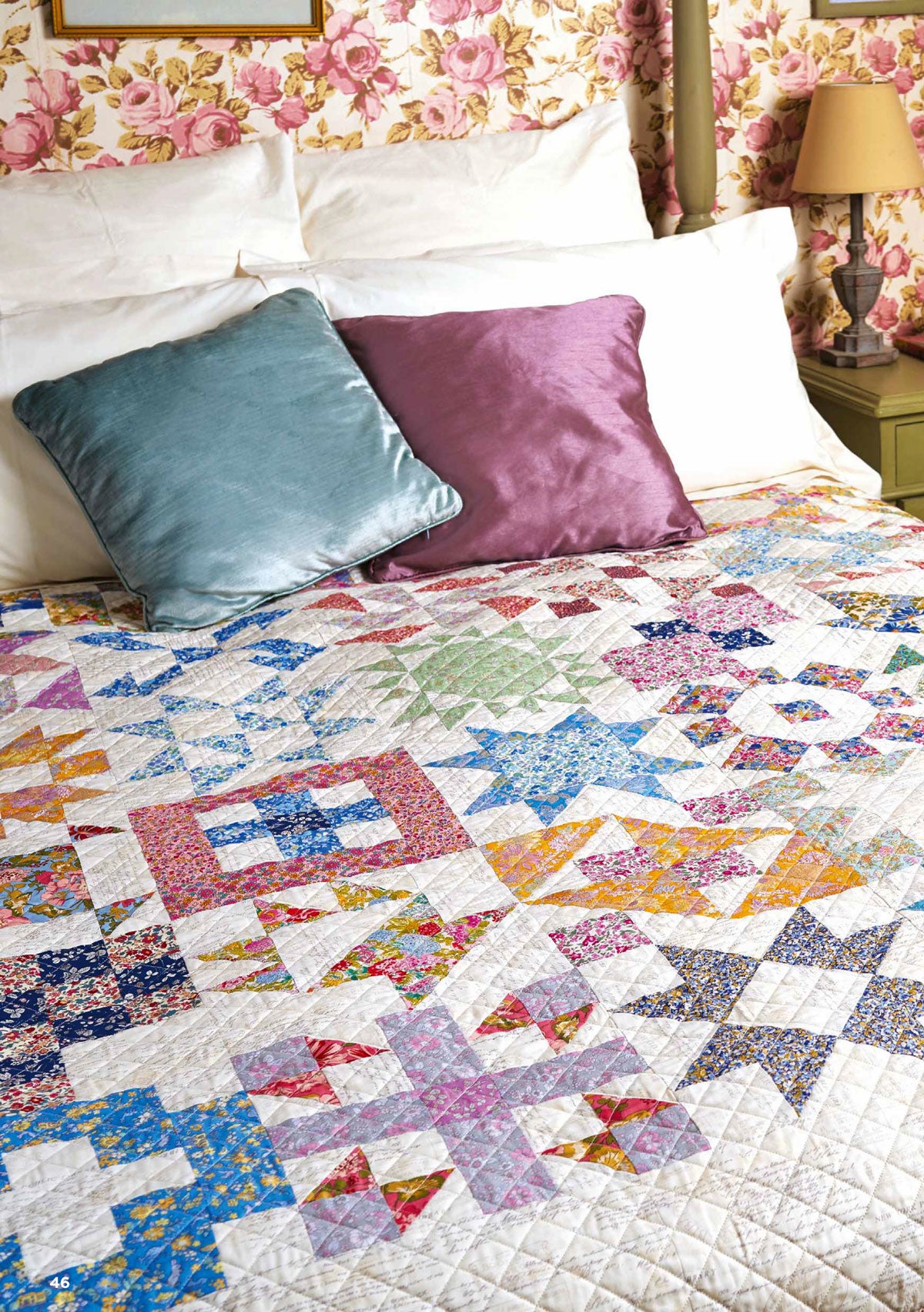 A quilt with various colorful geometric patterns displayed on a bed with decorative pillows.
