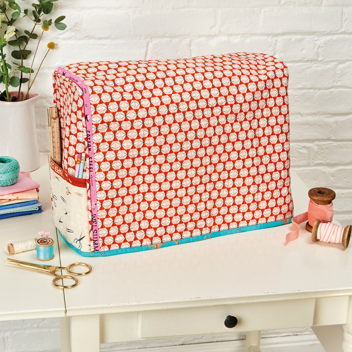 Fabric storage box with red and white pattern on a white surface with sewing supplies.