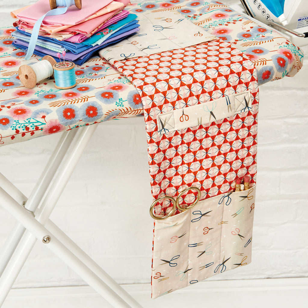Fabric with scissors pattern on a sewing table with fabric and tools.