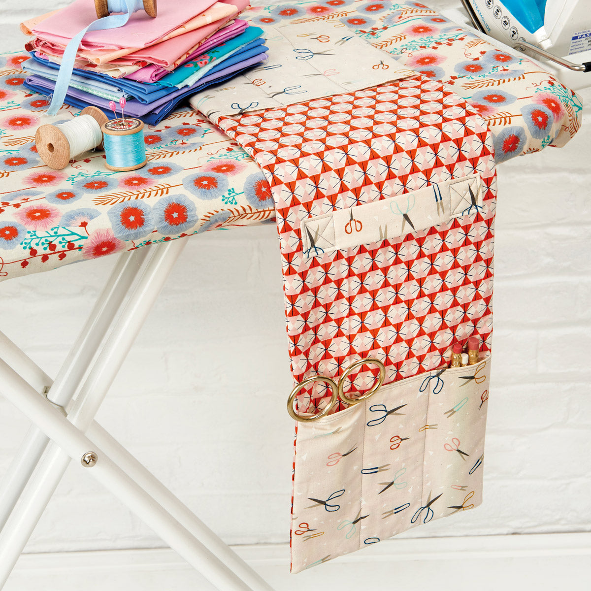 Fabric with scissors pattern on a sewing table with fabric and tools.