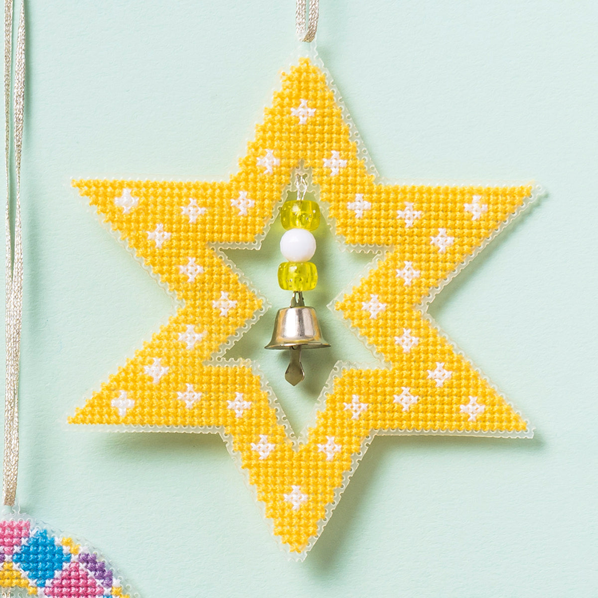 Star-shaped yellow beaded ornament with a bell on a light green background