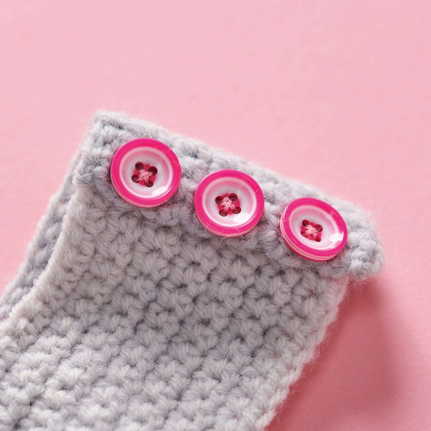Gray crochet fabric with pink buttons on a pink background