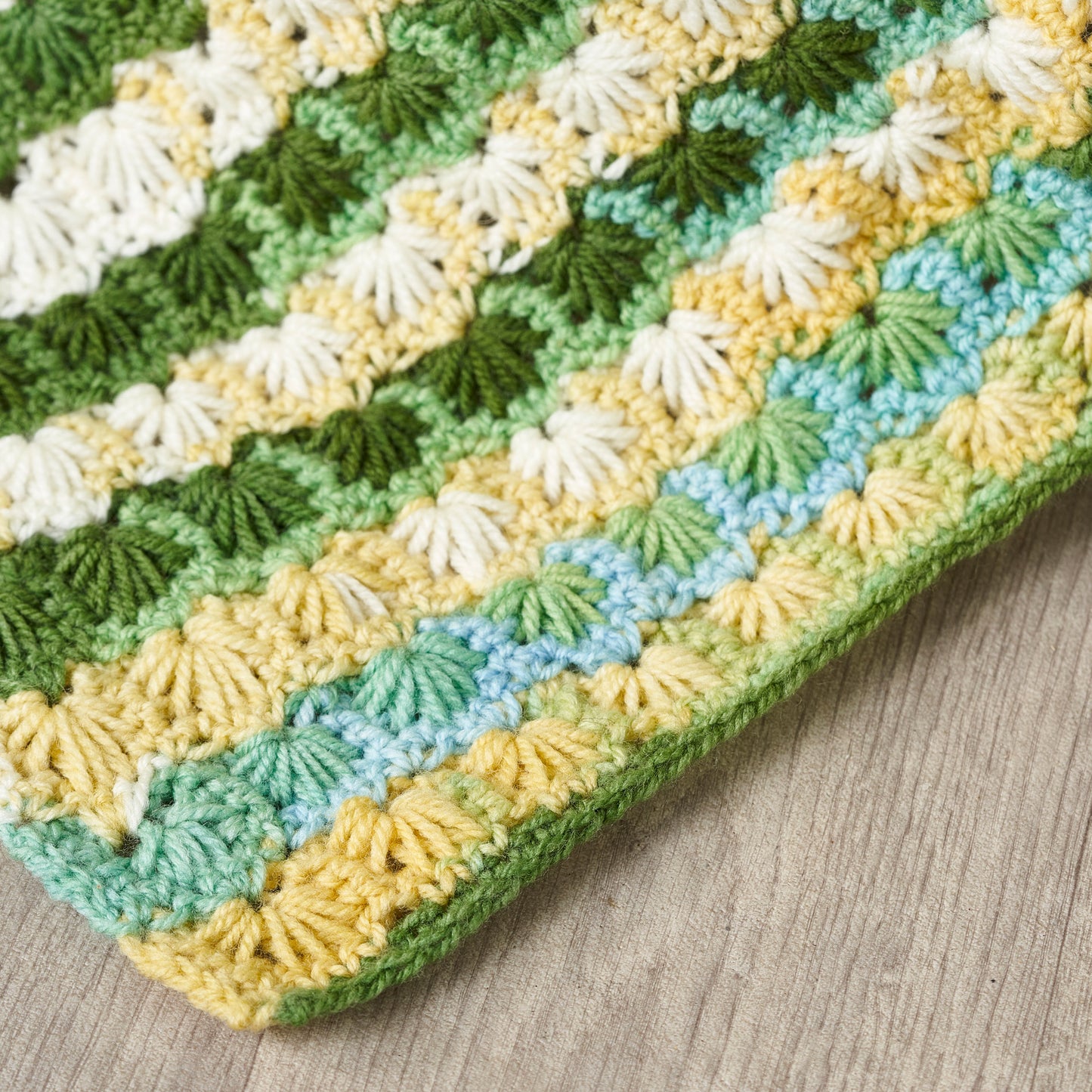 Crocheted blanket with green, yellow, and white pattern on a wooden surface
