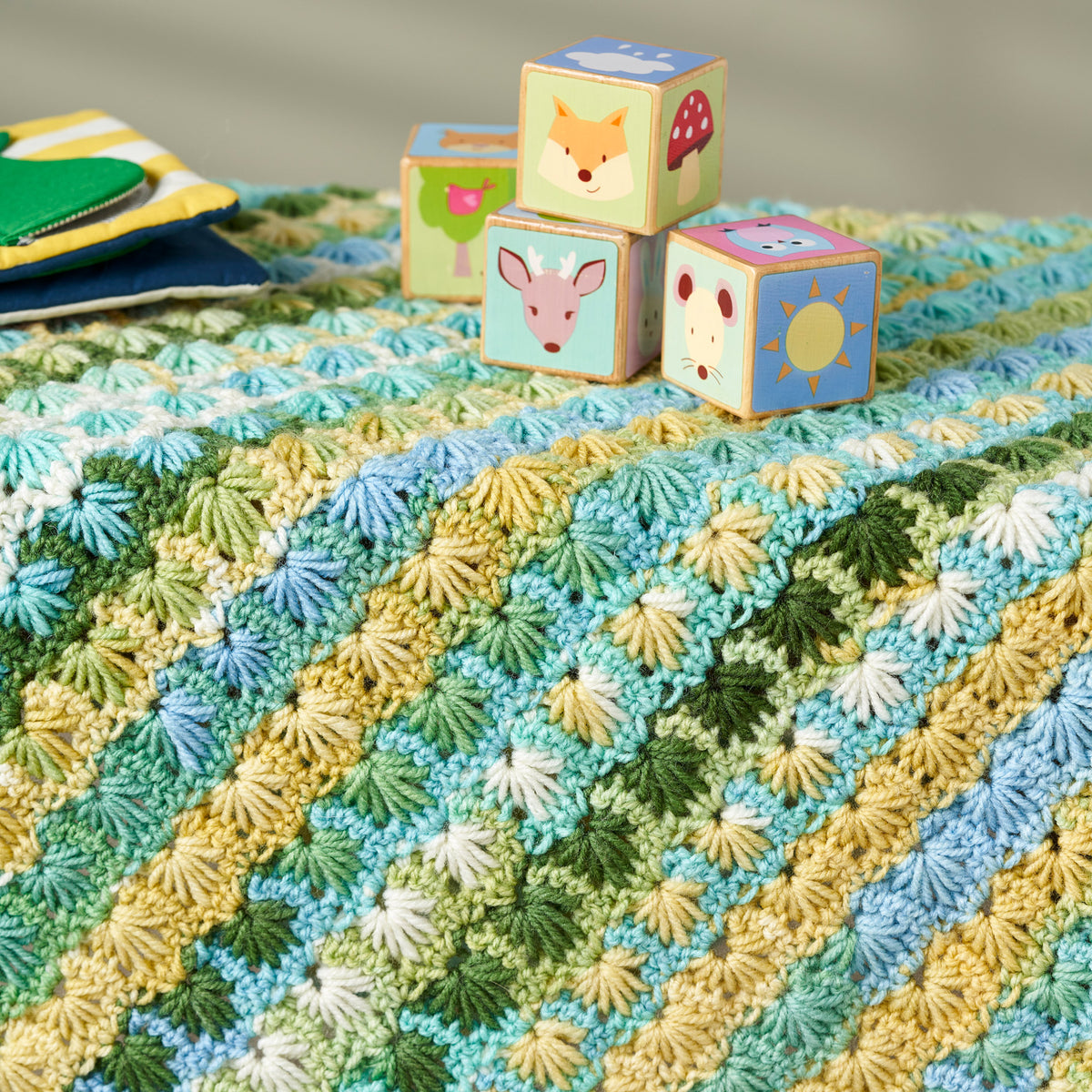 Crocheted blanket with a pattern of green, blue, and yellow, accompanied by children's blocks with animal designs.