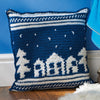 Crocheted pillow with house and tree design against a blue backdrop.