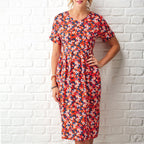 Woman wearing a colorful floral dress against a white brick wall.