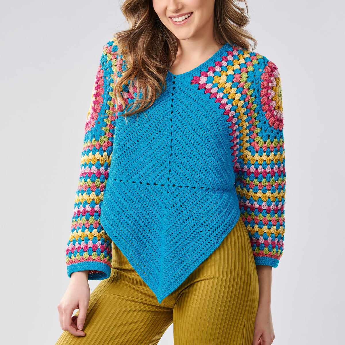 Woman wearing a colorful crochet sweater with a blue center on a light gray background