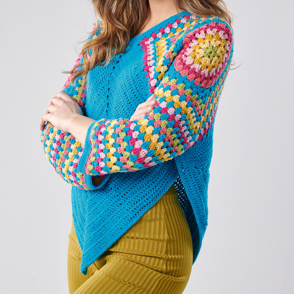 Colorful crocheted sweater with a geometric pattern worn by a person on a plain background