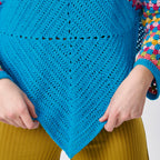 Close-up of a blue crochet shawl held by hands with a colorful background