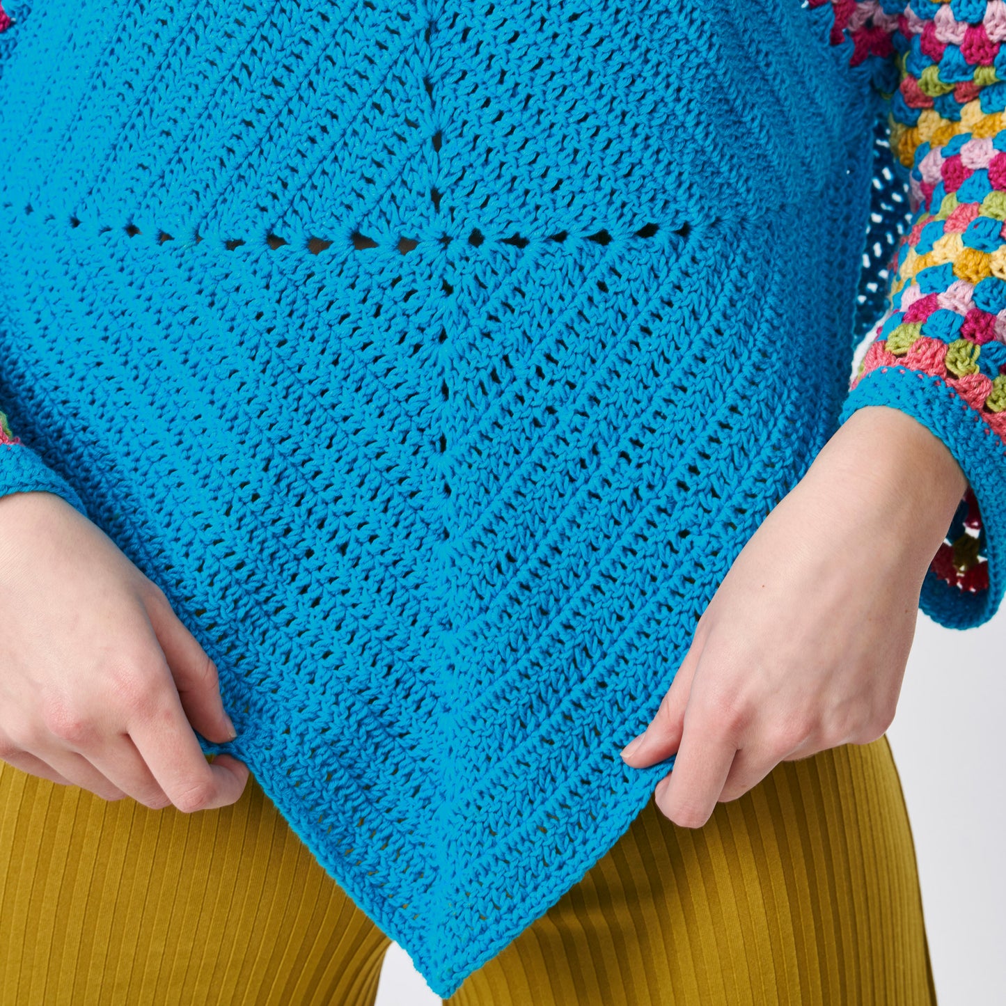 Close-up of a blue crochet shawl held by hands with a colorful background