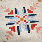 Quilt with geometric pattern in red, blue, and orange on a textured white background