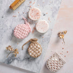 A collection of crochet patterns for soap pouches alongside a bar of soap with scattered Himalayan pink rock salt, displayed on a marble surface with a small brush and decorative flowers.