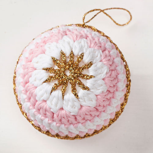 A crochet ornament featuring a white and pink spiral pattern, accented with a central gold star and edge. It hangs by a thin gold loop, exuding a festive feel.