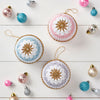 A collection of pastel-colored crocheted baubles with star patterns, displayed on a white surface, surrounded by other Christmas decorations.