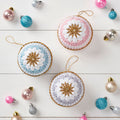 A collection of pastel-colored crocheted baubles with star patterns, displayed on a white surface, surrounded by other Christmas decorations.