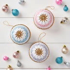 A collection of pastel-colored crocheted baubles with star patterns, displayed on a white surface, surrounded by other Christmas decorations.