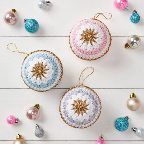 A collection of pastel-colored crocheted baubles with star patterns, displayed on a white surface, surrounded by other Christmas decorations.