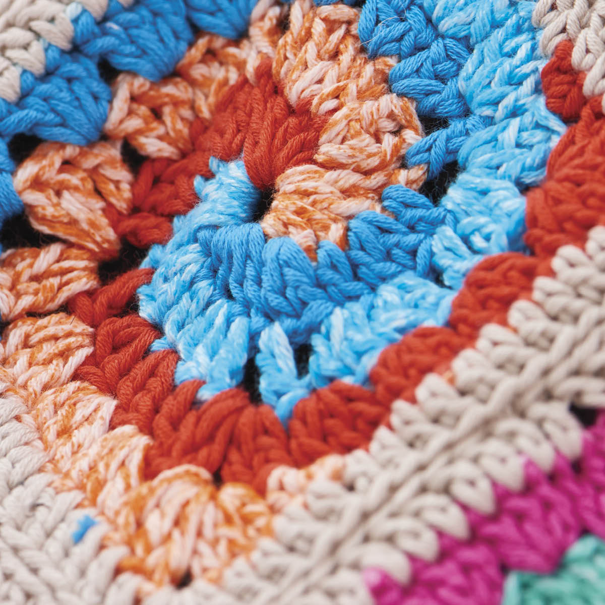 Close-up of a colorful crocheted fabric with blue, orange, and beige patterns.