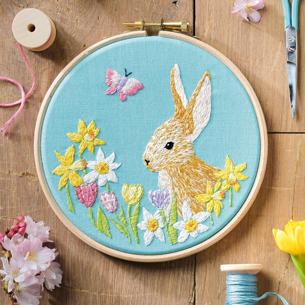 Embroidery hoop with a rabbit and floral design on a wooden surface.
