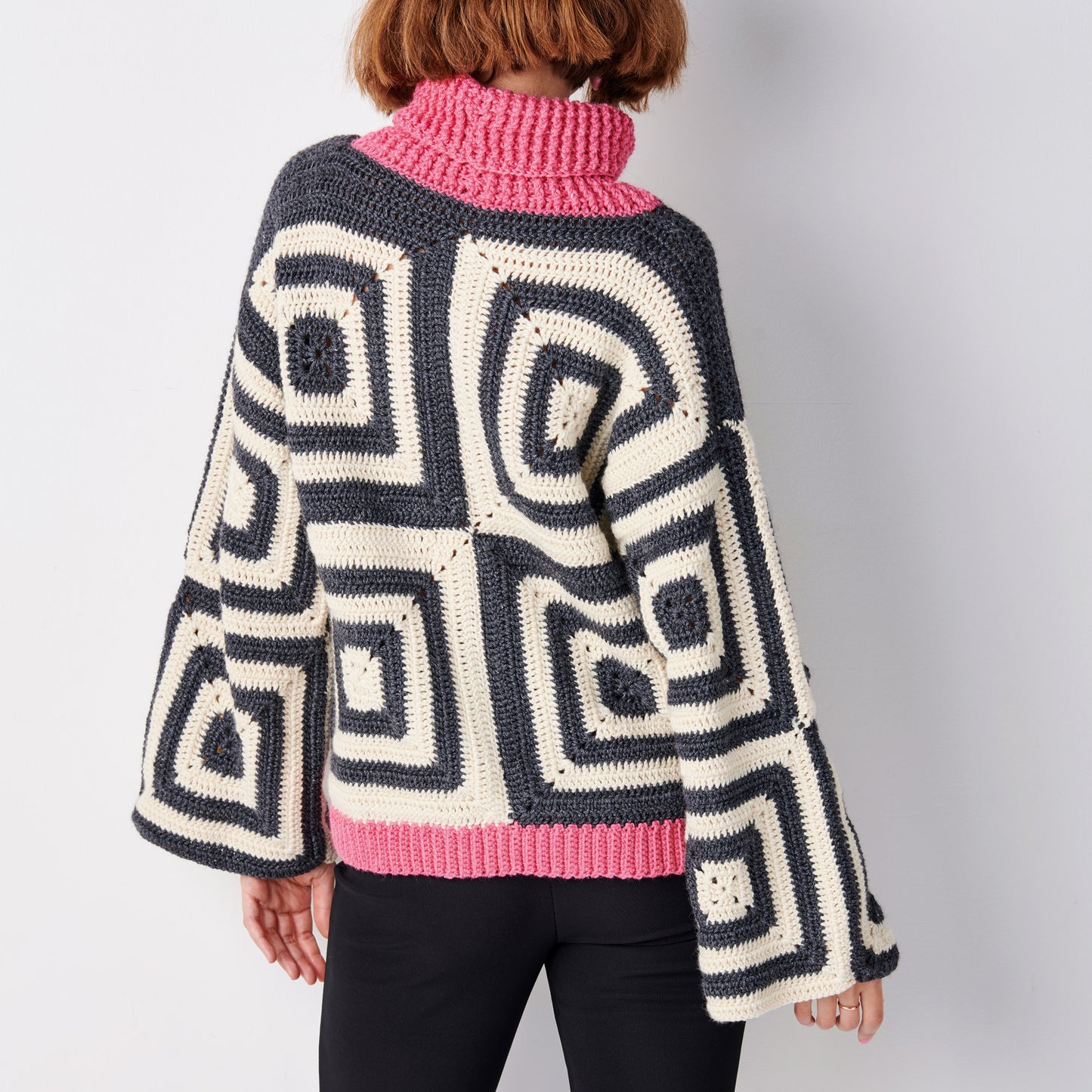 Person wearing a crocheted sweater with geometric pattern and pink turtleneck