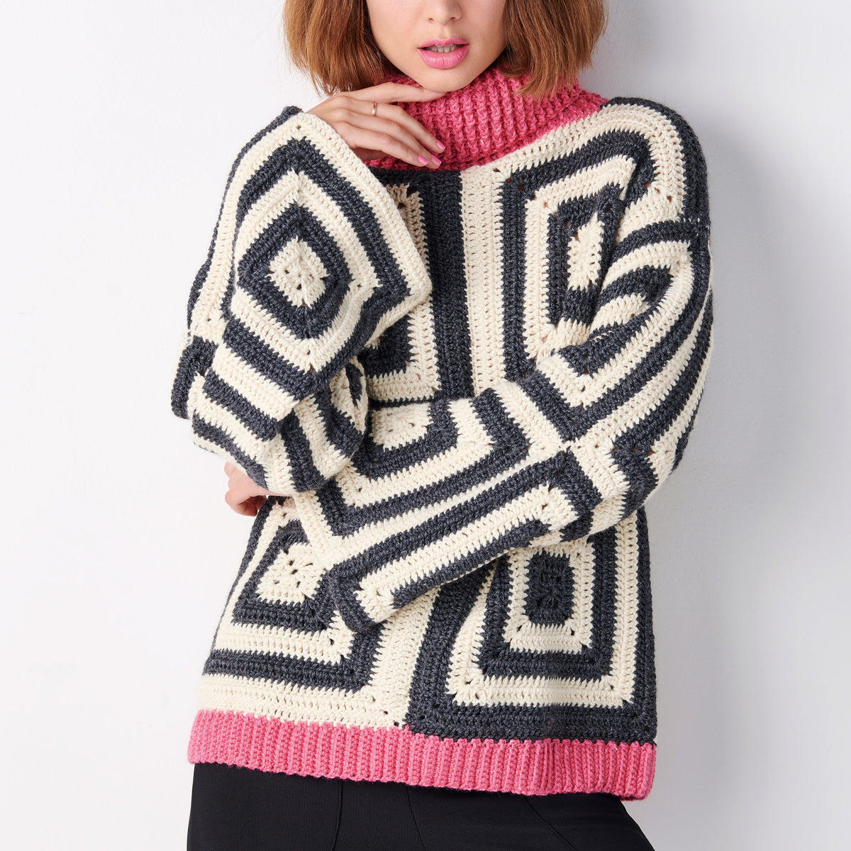 Person wearing a large, patterned crochet sweater with pink trim on a plain background