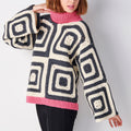 Person wearing a large, patterned sweater with geometric design on a plain background