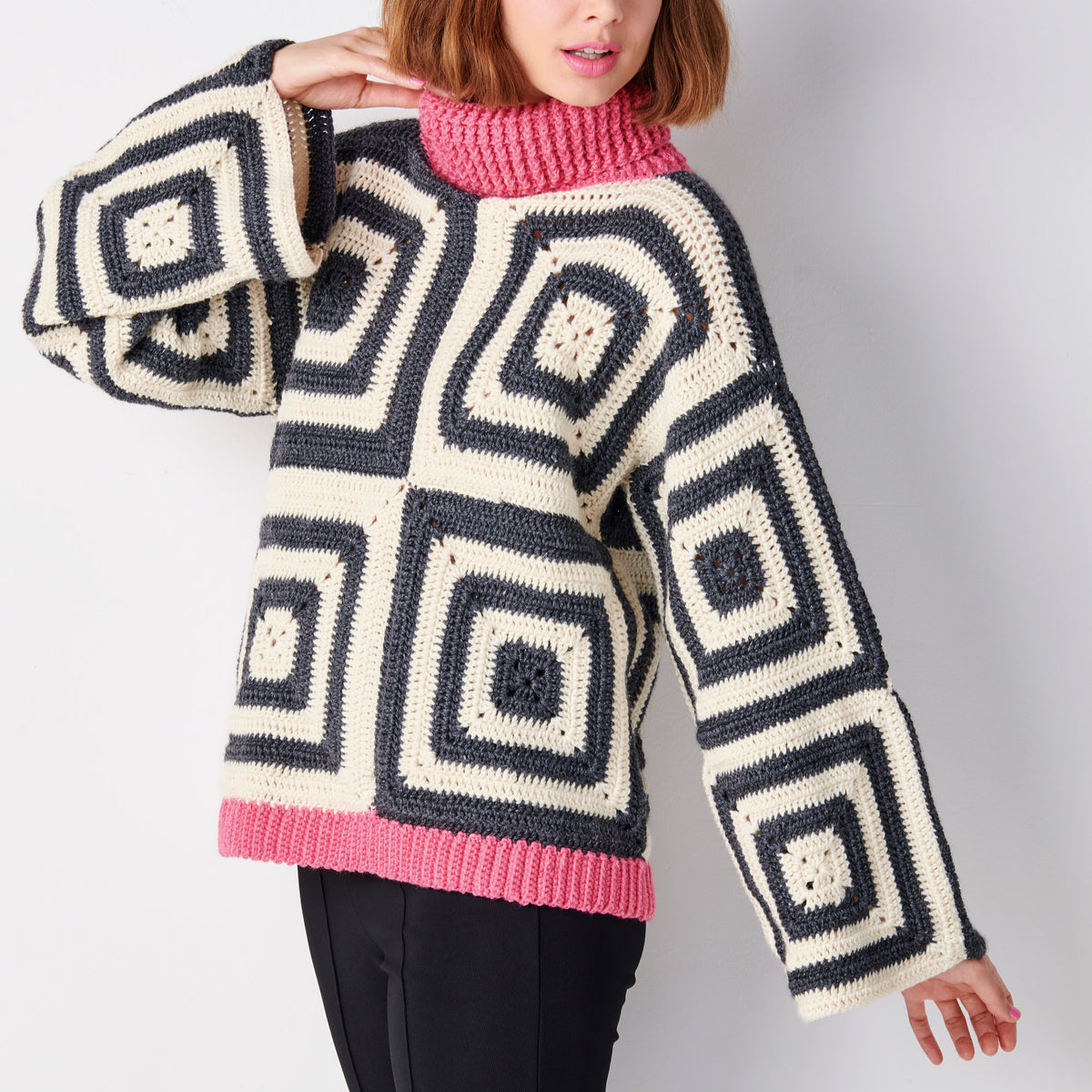 Person wearing a large, patterned sweater with geometric design on a plain background